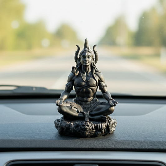 Statue of a meditating figure on a car dashboard with a blurred road and trees in the background
